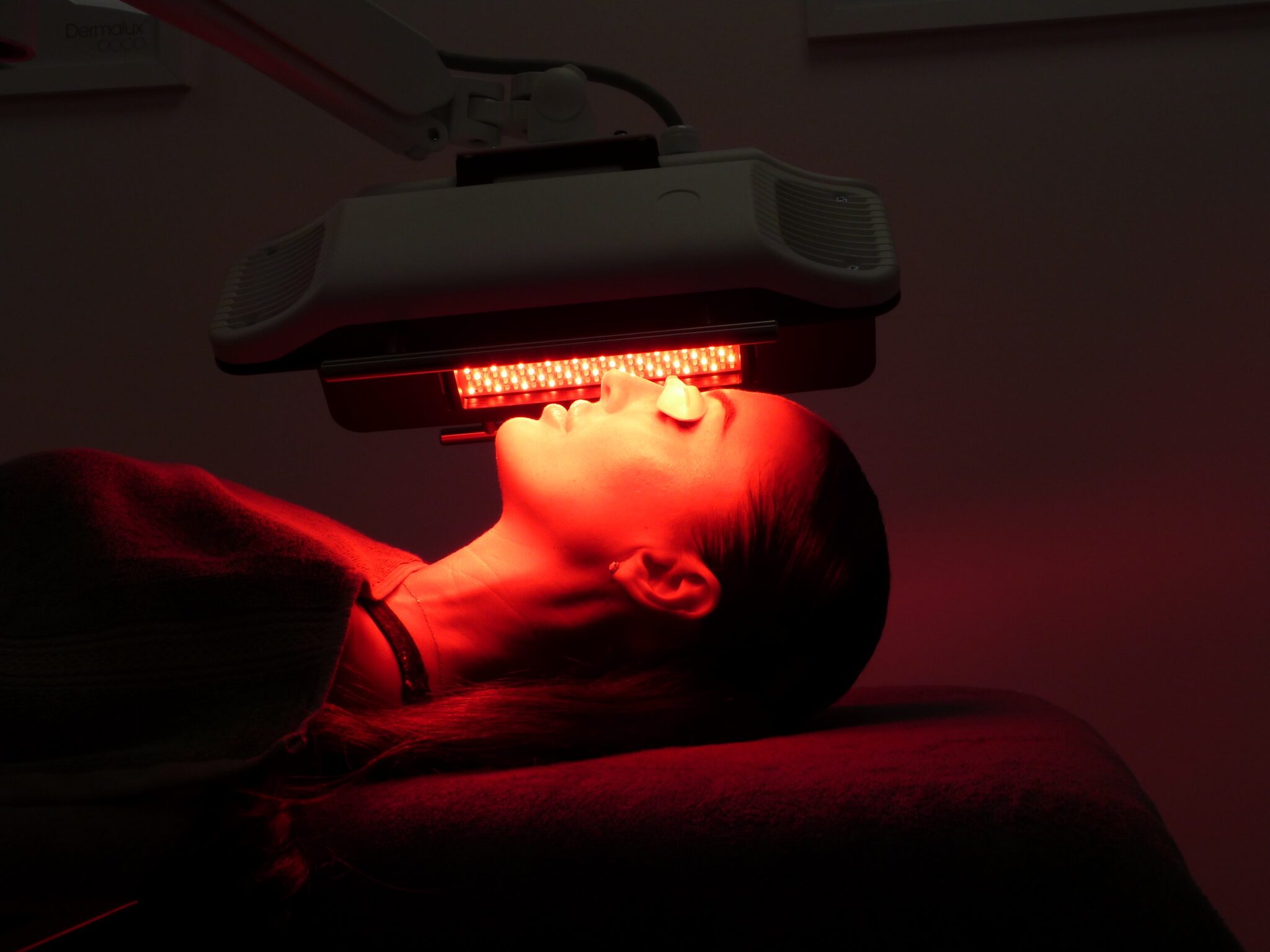 A client lying under a red LED phototherapy canopy during a skin treatment